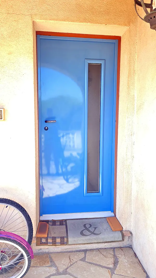 Porte blindée bi-coloration vue de l'extérieur : face laquée bleu azur et vitrage dépoli sur façade en enduit ocre