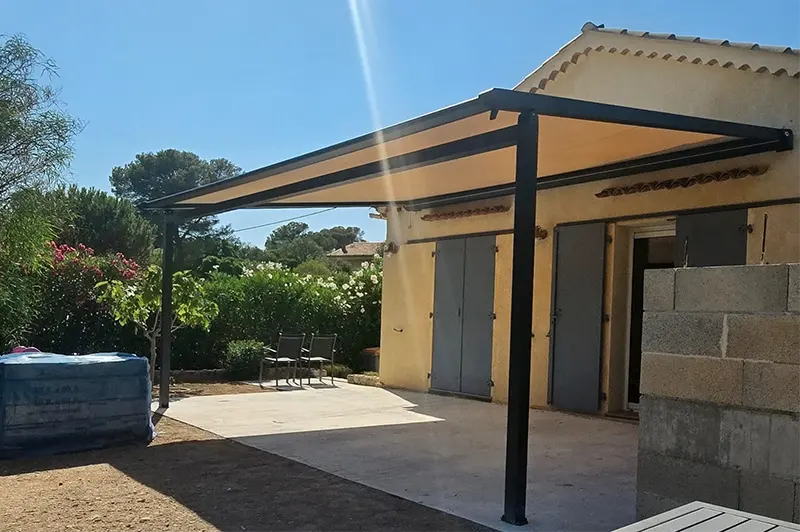 Vue de trois quarts de la pergola à toile beige sable et de sa structure aluminium anthracite sur poteaux