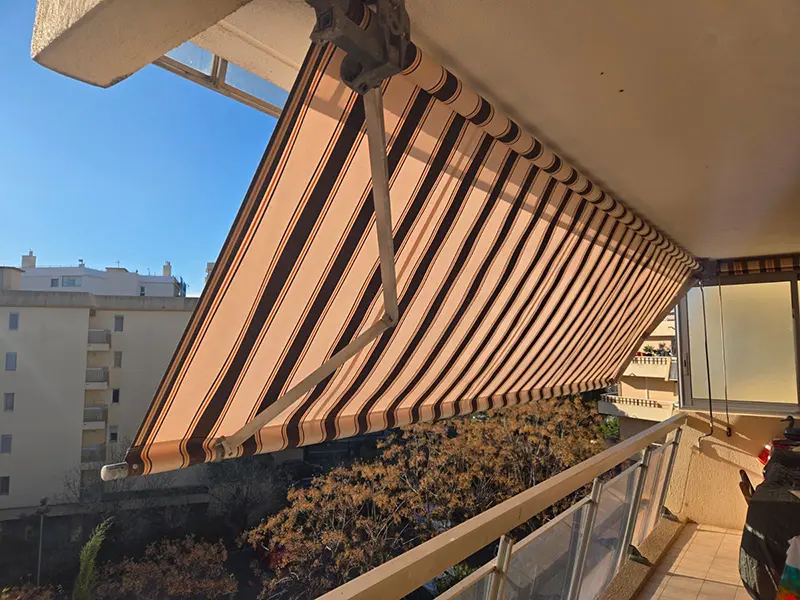 Le même store banne après remplacement de la toile par un tissu rayé beige et marron chocolat parfaitement tendu