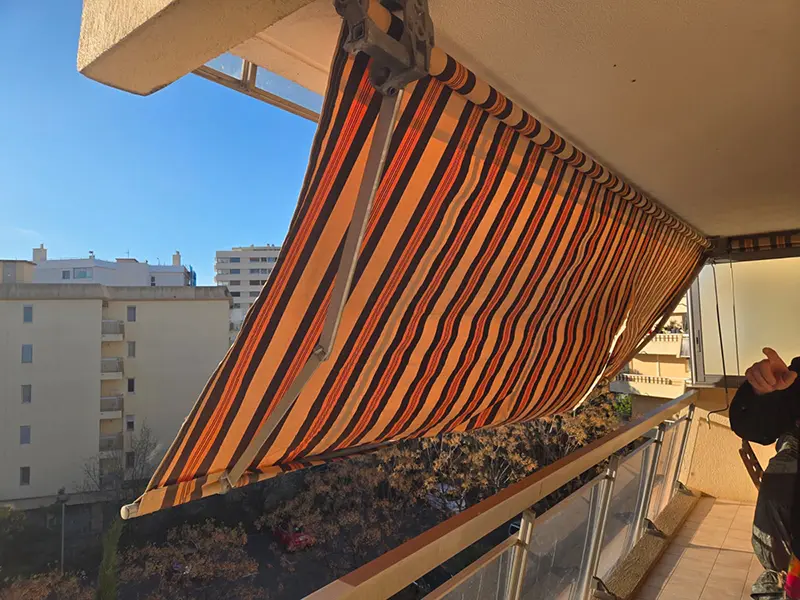 Store banne d'un balcon à Fréjus avant intervention : toile rayée ocre et brune décolorée et affaissée