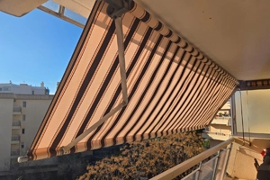 Store banne d'un balcon à Fréjus après remplacement de sa toile par un tissu rayé beige et marron